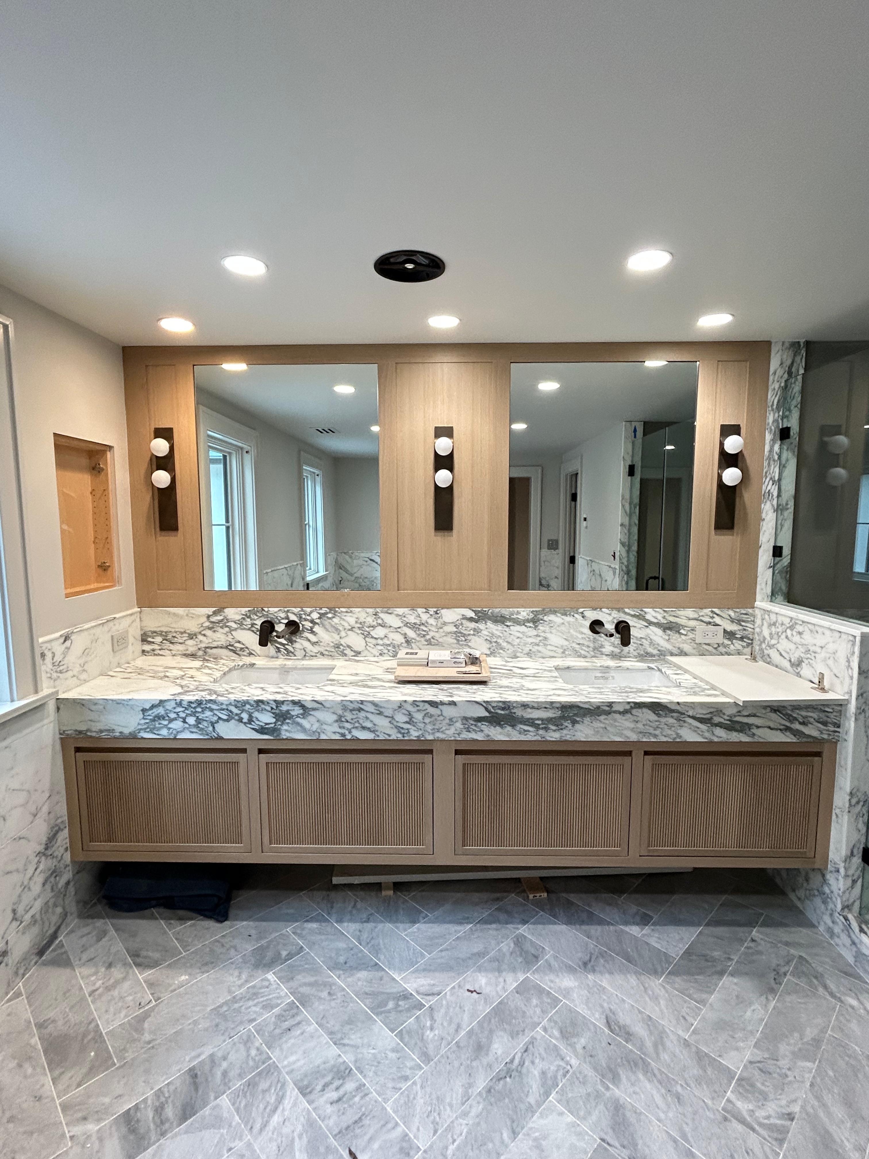 Luxury master bathroom with marble double vanity and herringbone tile floor by Mozy Construction